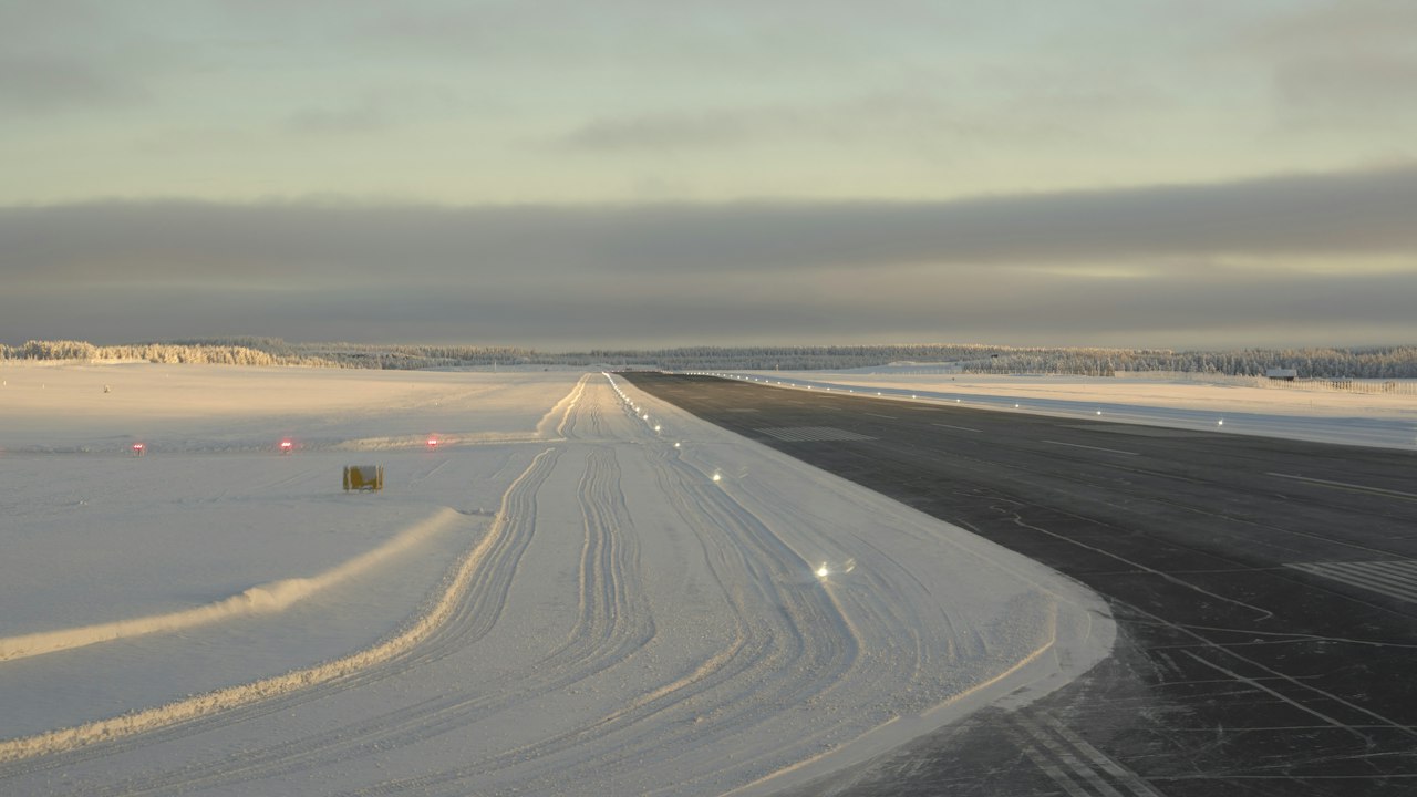 A snow-covered airport runway at first light, cleared lines running towards the horizon